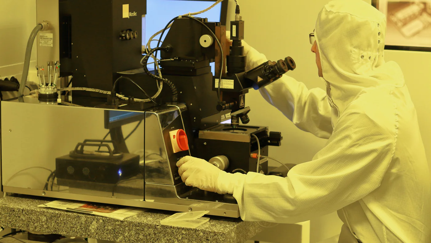 Medewerker in cleanroompak aan een microscoop in geel licht