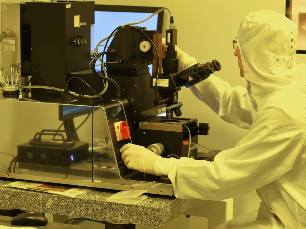 Medewerker in cleanroompak aan een microscoop in geel licht