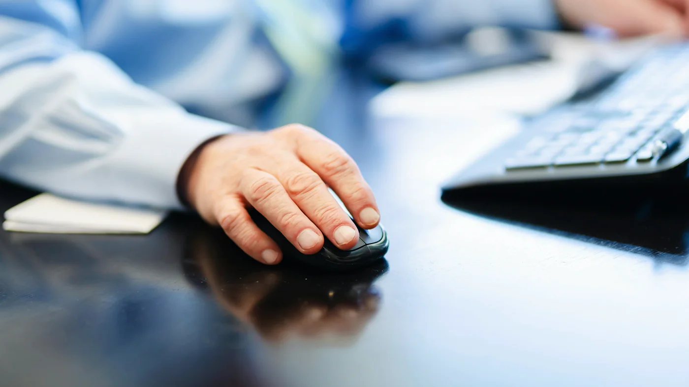 Hand op een muis naast een toetsenbord aan een bureau
