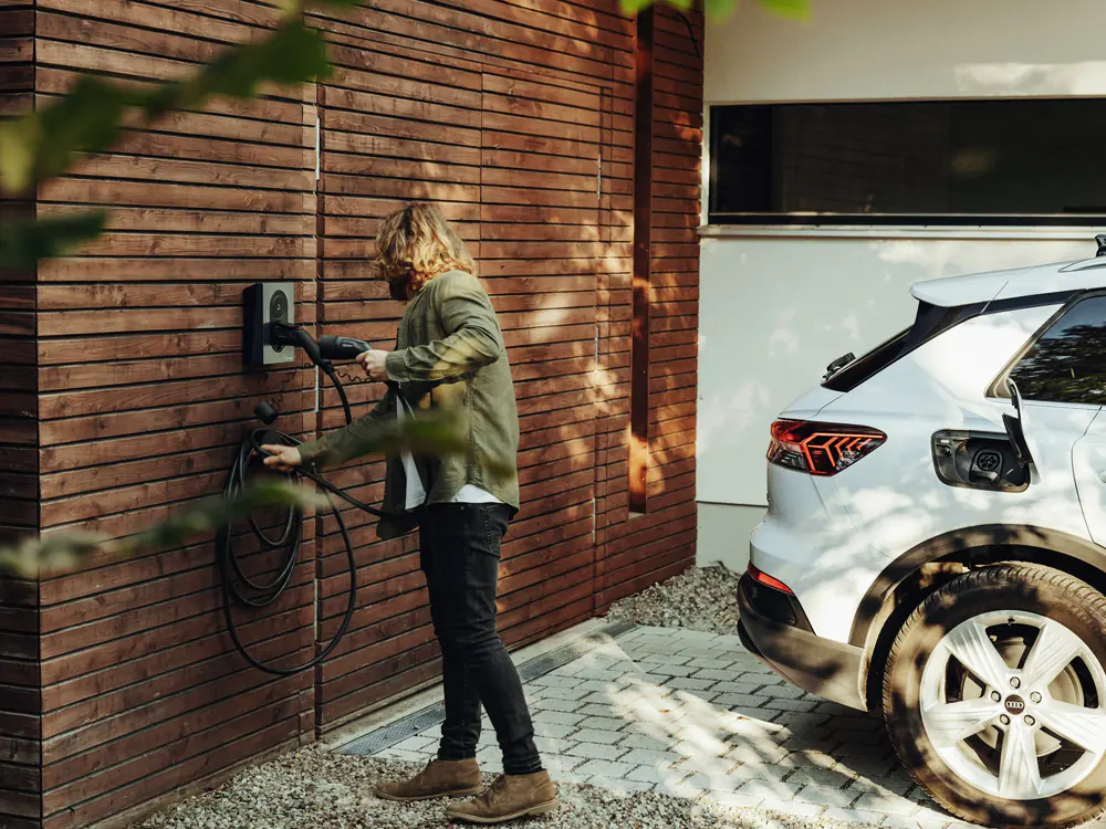 Laadpunt aan een bakstenen gevel met een elektrische auto ervoor