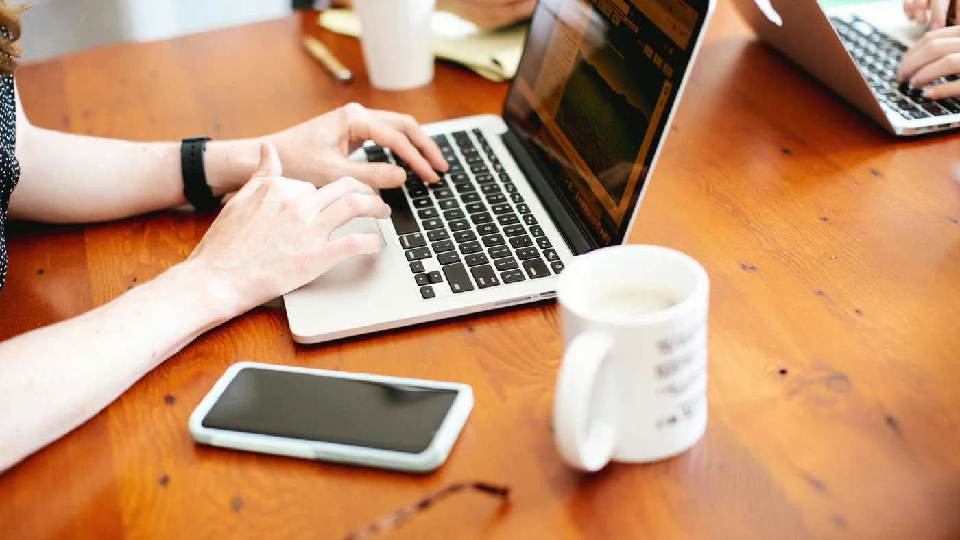 Laptop, telefoon en koffie op een houten bureau