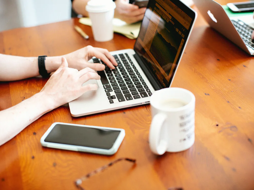 Laptop, telefoon en koffie op een houten bureau