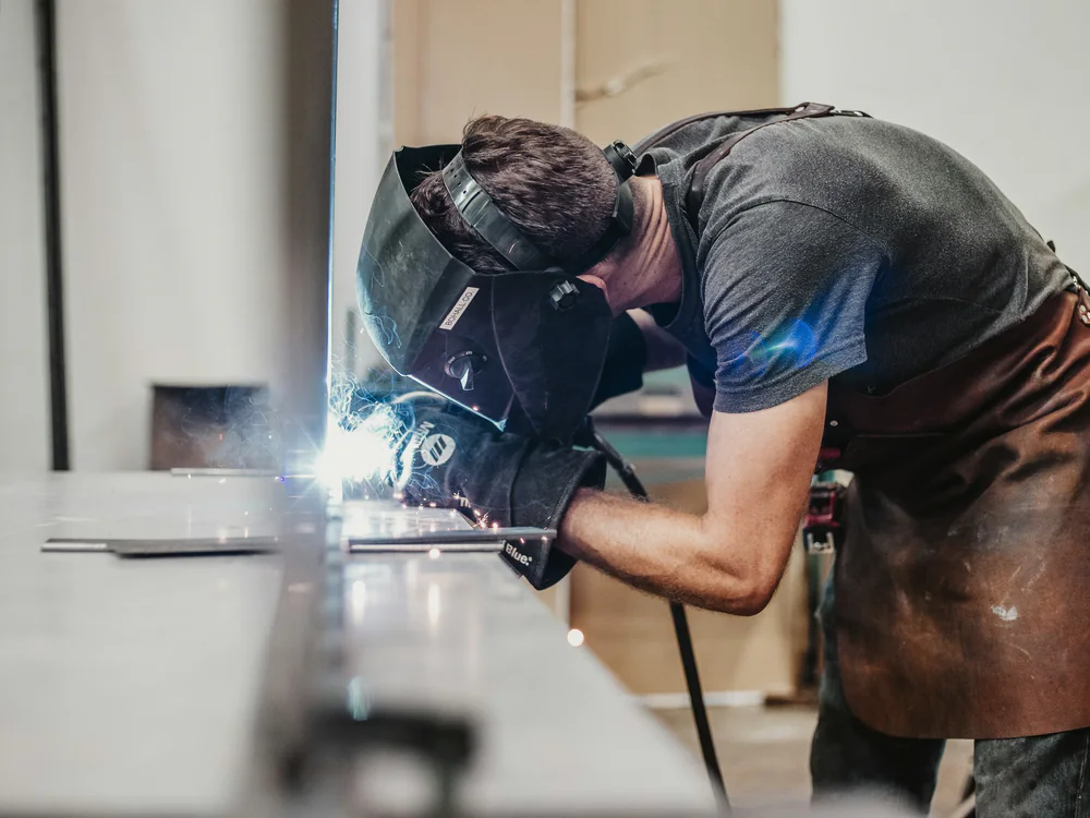 Lasser buigt over een werkbank en last een stalen profiel
