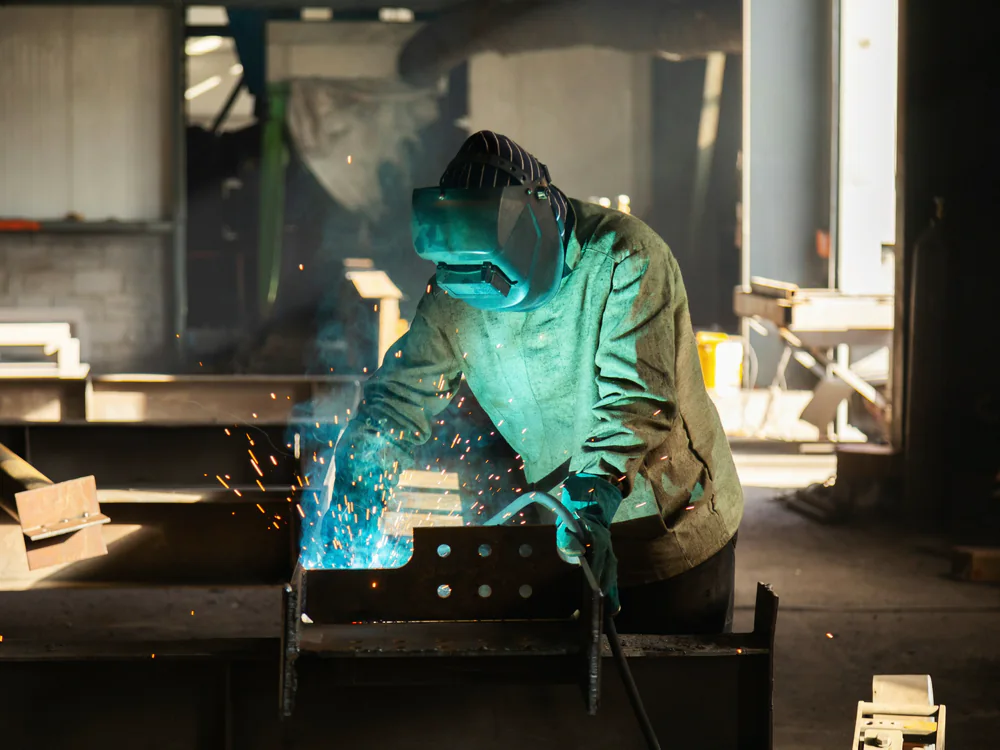 Lasser aan het werk in een metaalwerkplaats vol lasrook en licht