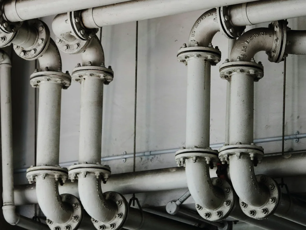 Grijze leidingen met flenzen langs een wand