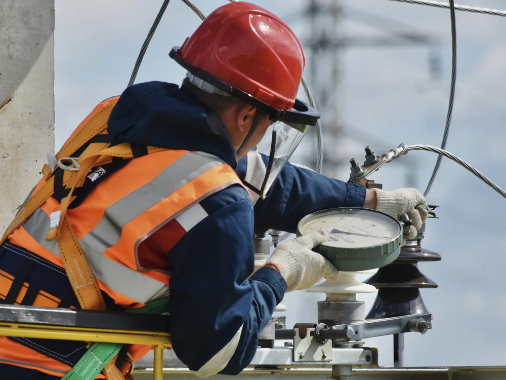 Lijnwerker met helm en harnas werkt aan een mast