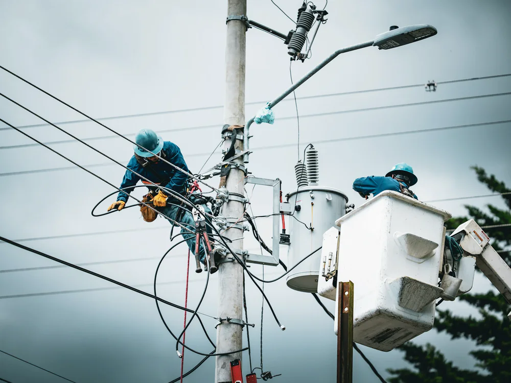 Twee lijnwerkers in een hoogwerker bij een elektriciteitsmast