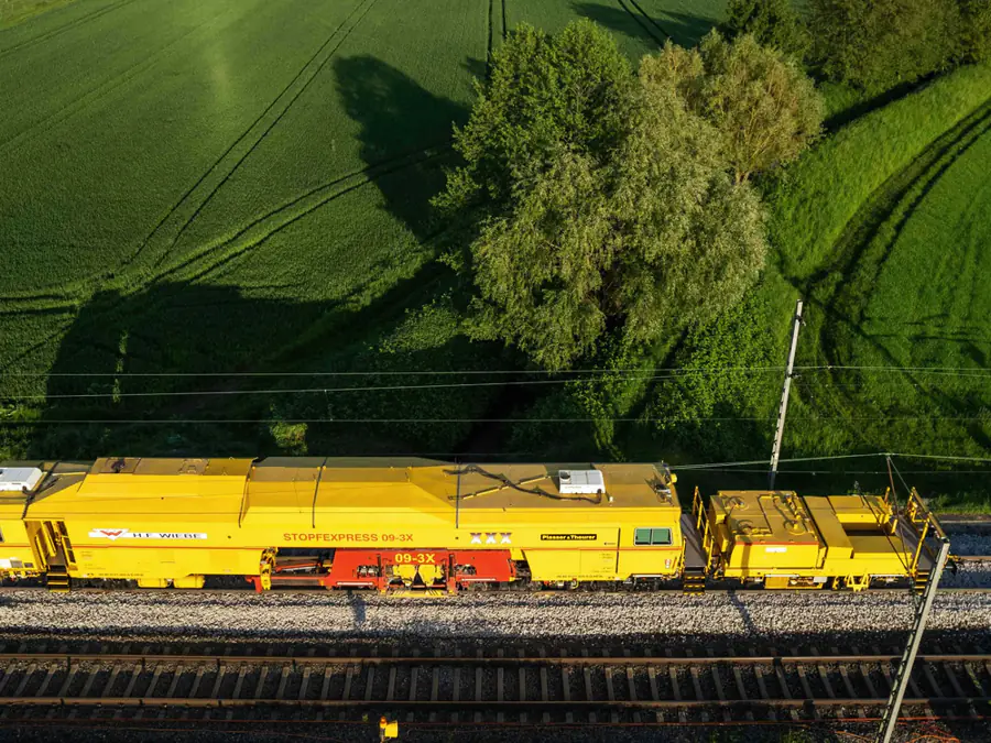 Gele onderhoudstrein op het spoor tussen groene velden, van bovenaf