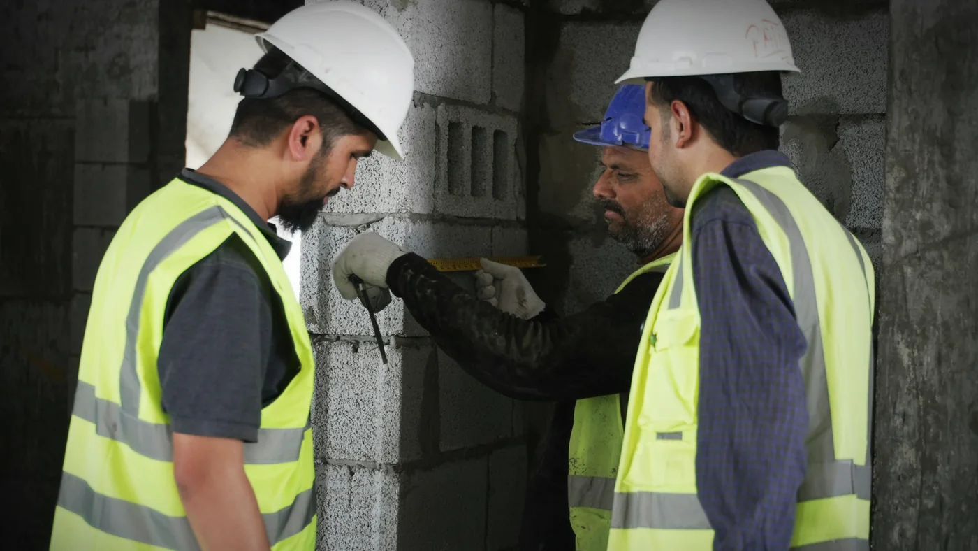 Twee vakmensen met helm en hesje controleren een wand op de bouwplaats