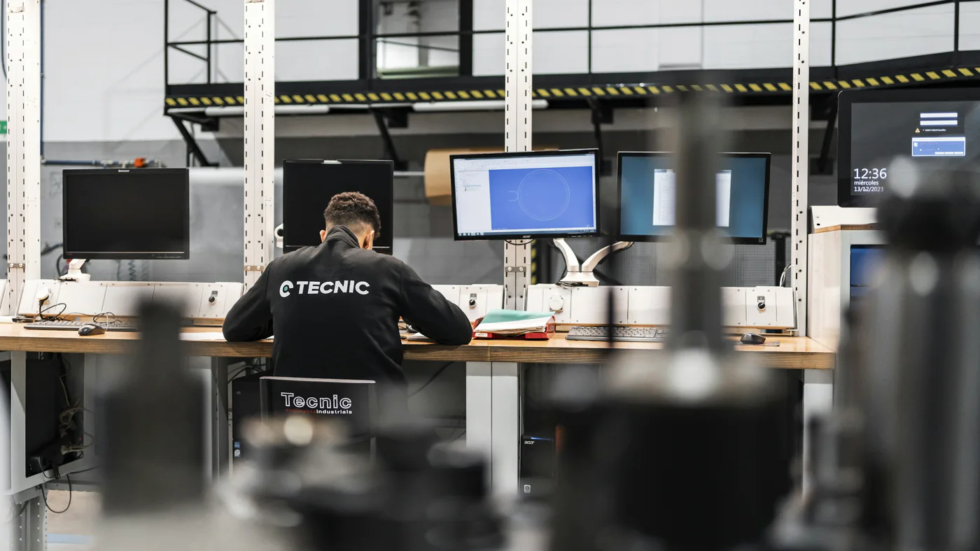 Technicus achter een computer in een werkplaats met machines